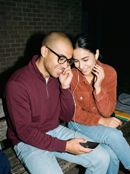 Two students sharing earphones on a campus bench