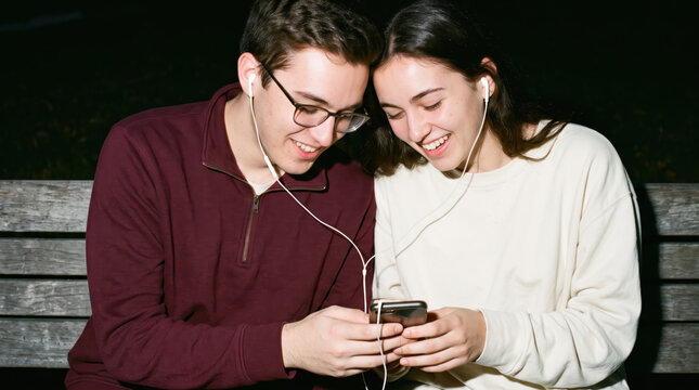 Two students sharing earphones on a campus bench