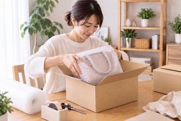 梱包したハンドバッグを段ボール箱に入れる女性