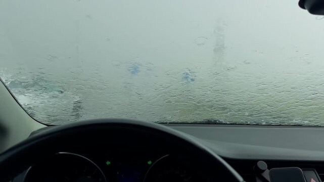 Car interior facing rain soaked windshield during heavy storm with blurred road view and dashboard in foreground