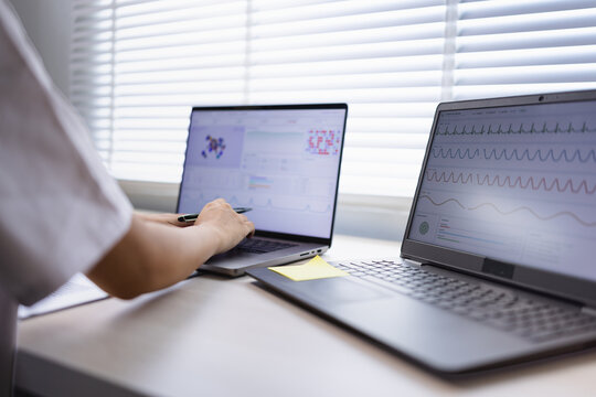 A professional medical researcher or doctor analyzing patient data charts and health statistics on laptop screens in a modern hospital office.