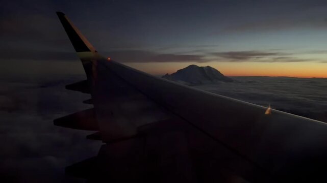Airplane Wing Flying over Clouds and Snow-Capped Mountain Peak at Sunset