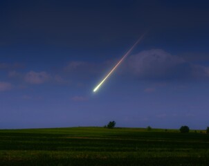 Meteor flared over green fields in the evening sky. Landscape with bright fireball. Meteorite burned up in the atmosphere. © Nazarii