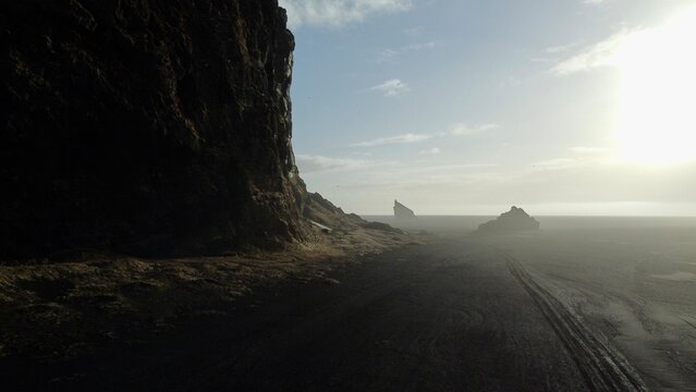 Dramatische steile Felswand an einem schwarzen Sandstrand im Gegenlicht, Island
