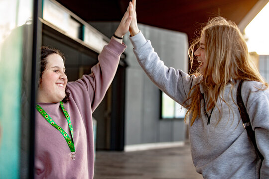 Two young women standing inside the metro station doing mid&ndash;high-five smiling at each other