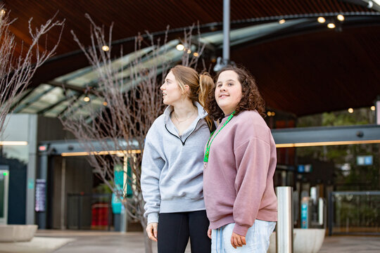 Two young women standing on an urban street sharing a warm, friendly moment