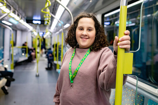 Teenager smiling while standing and holding a support pole inside a modern metro train