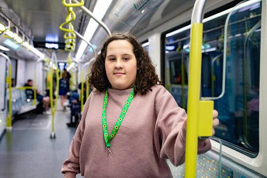 teen girl with curly hair standing and holding a support pole inside a modern metro train