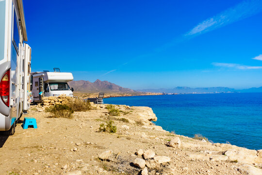 Camping by the water at a scenic location with two RVs parked near the shore during a sunny day