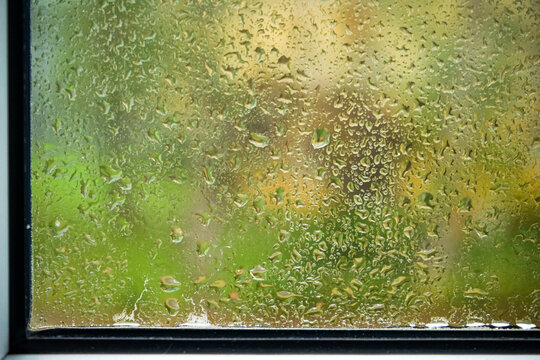 Raindrops on a window pane showing greenery n the background on a cloudy day
