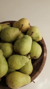 Fresh green pears piled inside a dark rustic wooden bowl on a clean white surface. Ideal for culinary commercials, healthy eating campaigns, nutrition blogs, organic farm promotions, and cooking tuts