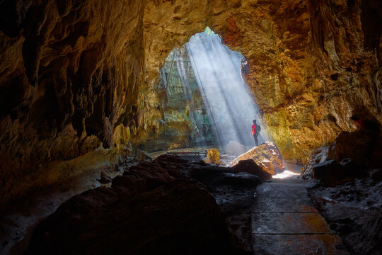 View of a person standing in the Goa Terawang Eco Park cave, illuminated by sunbeams streaming through a ceiling opening, surrounded by limestone in Todanan, Central Java, Indonesia.