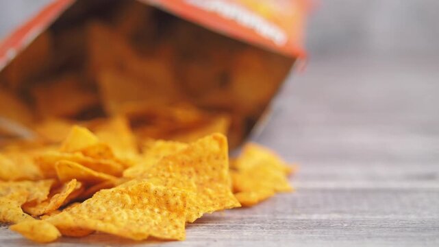 Crispy corn tortilla chips falling out of red snack bag on wooden table in close up view