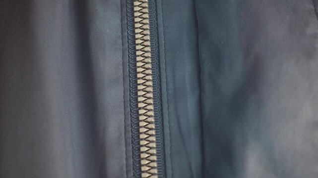 Person zipping up silver metal zipper on navy blue nylon jacket fabric