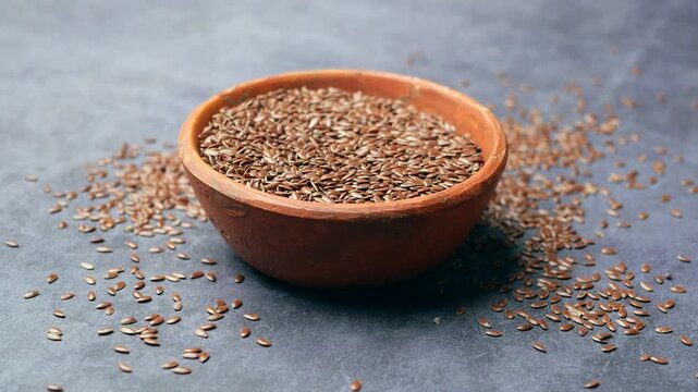 Close up shot of flax seeds in a terracotta bowl on a dark background with scattered seeds around
