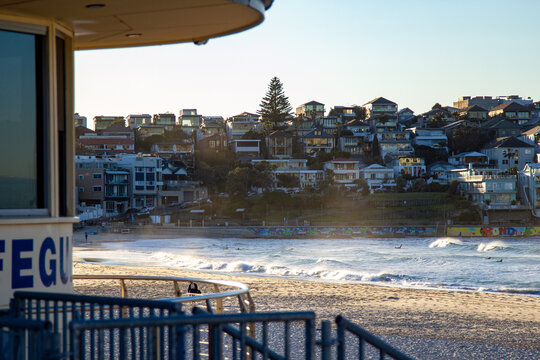 Lifeguard tower overlooking surfers, breaking ocean waves, sandy beach and coastal hillside town