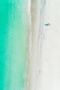 Overhead aerial of person walking on white sandy beach with turquoise ocean