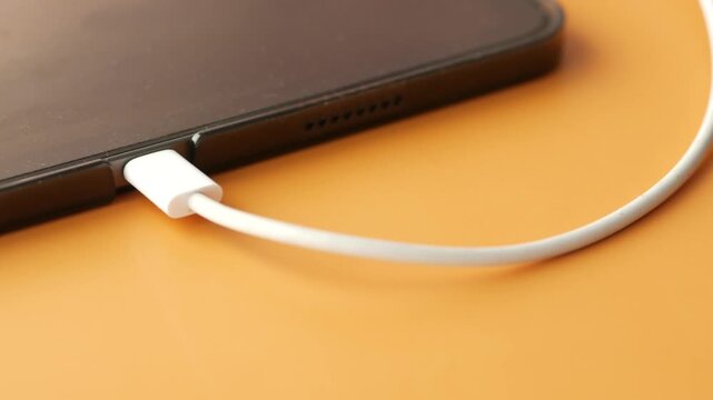 Close up view of tablet computer charging with white cable on orange background, showcasing modern technology and charging process