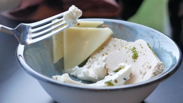Close up of fork picking up creamy cheese from bowl with halva and olives