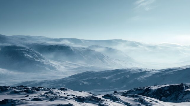 A vast snowy mountain range under a clear blue sky with soft mist drifting between the peaks