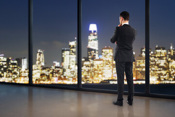 Obraz premium Businessman standing by a window at night, viewing a glowing city skyline while reflecting on corporate strategy, research, and the future.