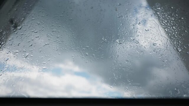 Raindrops bead and trickle along an inclined glass skylight under an overcast sky. Natural daylight illuminates condensation patterns ideal for home maintenance and weatherproofing concepts.
