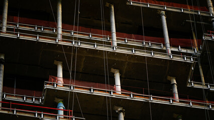 High rise building under construction with temporary work platforms, concrete columns and protective safety netting, illustrating construction safety, structural engineering and urban development © belavinstock