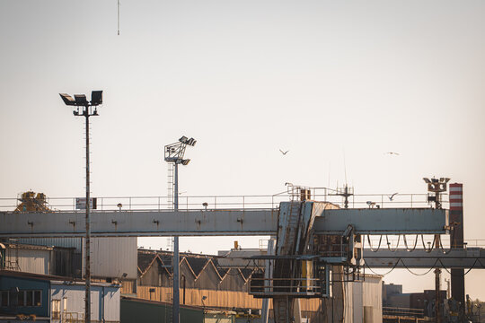 View of industrial shipyard infrastructure with a large gantry crane, metal structures, and seagulls flying against a clear sky in Pula, Istria County, Croatia.