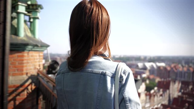 Young woman stands on a historic tower observation deck admiring the panoramic view of a European old town