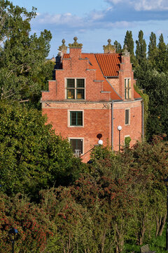 Historic red brick building with stepped gables surrounded by green trees and parkland in Gdansk, Poland