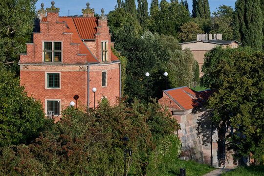 Historic red brick building and stone fortification wall surrounded by trees in Gdansk, Poland