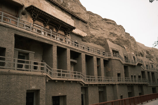 View of Mogao Caves featuring intricate wooden balconies and walkways carved into the cliff face under a soft overcast sky in Jiuquan, Gansu, China.