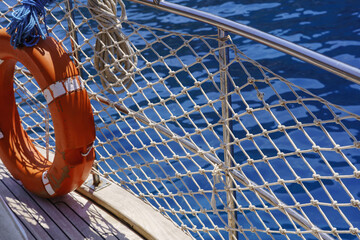 Orange lifebuoy and rope safety net on boat deck near blue sea © dddoria