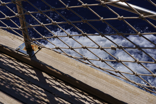 Rope railing net and wooden boat deck above dark blue sea wake