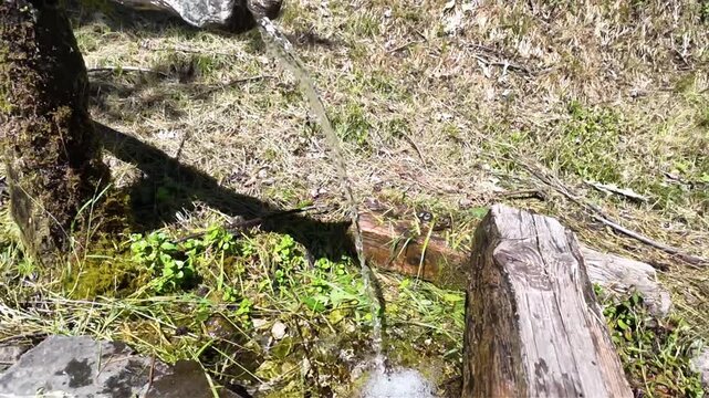 A relaxing slow-motion shot of a traditional mountain fountain. The water is fresh and crystal-clear, featuring suspended droplets and unique reflections, all set amidst the greenery and tranquility 