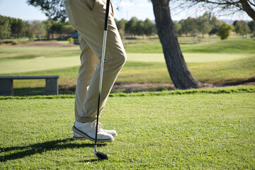 Close-up of a golfer's legs, shoes and iron addressing the ball, detail shot capturing technique and precision on the fairway. © Gonzalo
