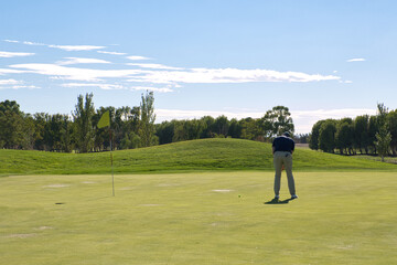 Obraz premium Golfer bending over to line up his putt near the flag, concentration and precision in a candid moment on the green.