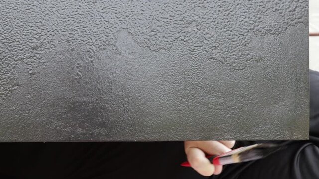 close-up video of a man painting a weathered metal door with black protective coating, showing diy home renovation, rust prevention, surface restoration and exterior maintenance