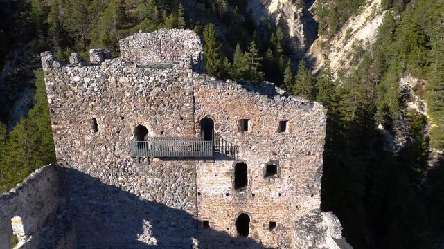 castle ruin stone facade arched window openings modern viewing balcony railing belfort castle broken battlements golden afternoon light mountainside albula valley aerial drone close pass graubunden
