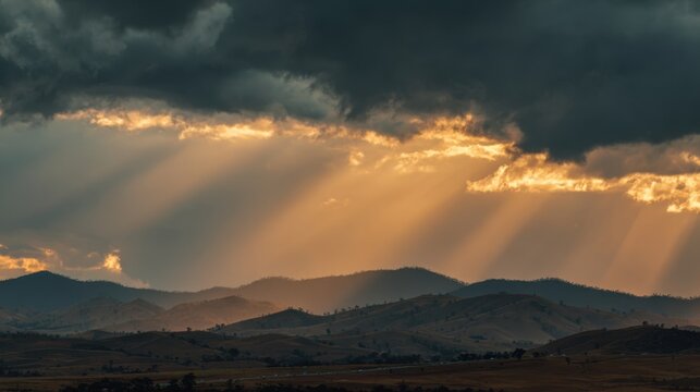 Dramatic sunset landscape with golden sun rays piercing through dark stormy clouds over rolling hills