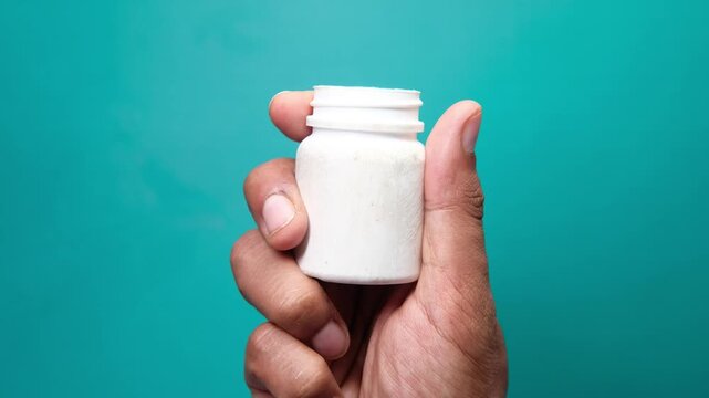 Close up view of hand holding medicine bottle on light green background, clean and minimal medical concept