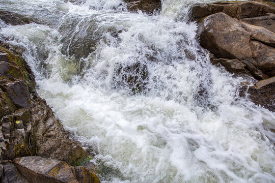 White foaming water rushing over stream rocks texture background