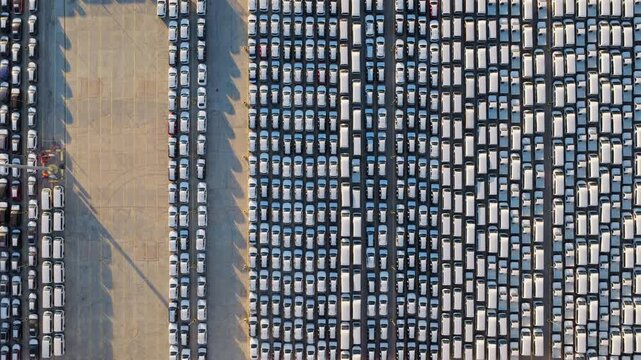 Top down aerial view showing brand new cars parked in neat rows in a lot, waiting for shipment and export at an industrial port terminal. Automotive industry and mass production concept