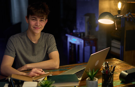 Teenage student learning at home with books and laptop computer. Online school and education, sitting at desk late night