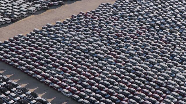 Thousands of new cars parked in neat rows at a dealer distribution facility or factory parking lot, awaiting distribution and sale in the automotive market, showcasing industrial overproduction