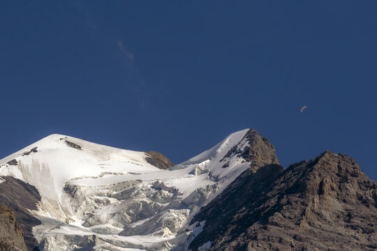 View of the snow-covered peak of the Jungfrau mountain under a clear blue sky with a small paraglider visible in the distance in Interlaken, Canton of Bern, Switzerland.