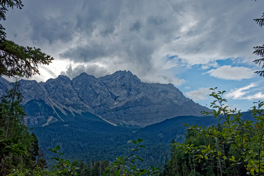 Mountain View Through Alpine Forest Framed by Dramatic Cloudy Sky Near Zugspitze