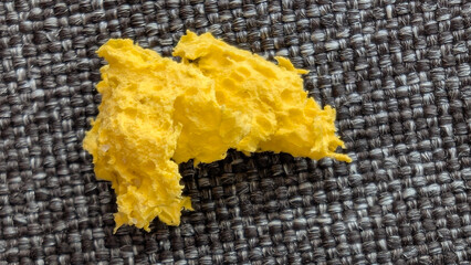 A porous yellow sponge fragment rests on a dark woven fabric surface, creating a striking color and texture contrast. © Beautiful talkers
