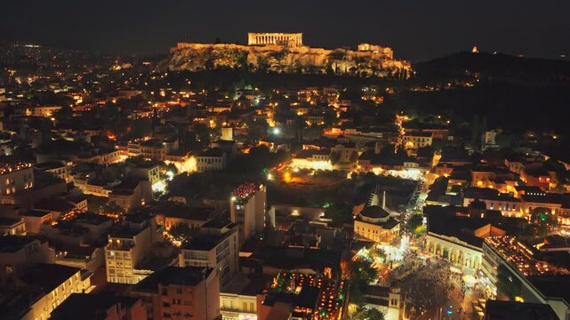 Breathtaking aerial footage flying over the illuminated cityscape of Athens at night, capturing the ancient Acropolis and Parthenon standing majestically over the modern urban sprawl of Greece