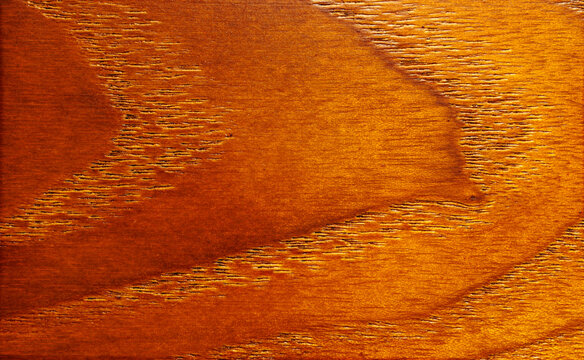 High res texture of a varnished mahogany wood panel showcasing rich orange grain patterns.